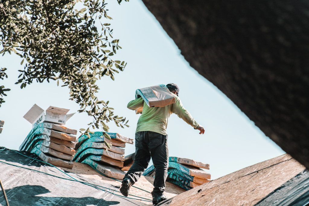 Roofer carrying shingle bundles across a roof